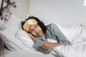 Is Insomnia Genetic? Cozy scene of a woman lying in bed with an eye mask, contemplating and relaxing.