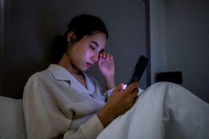 A woman rubs her eyes while reading from an electronic device