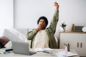 A man yawns with a large stretch while seated at a desk