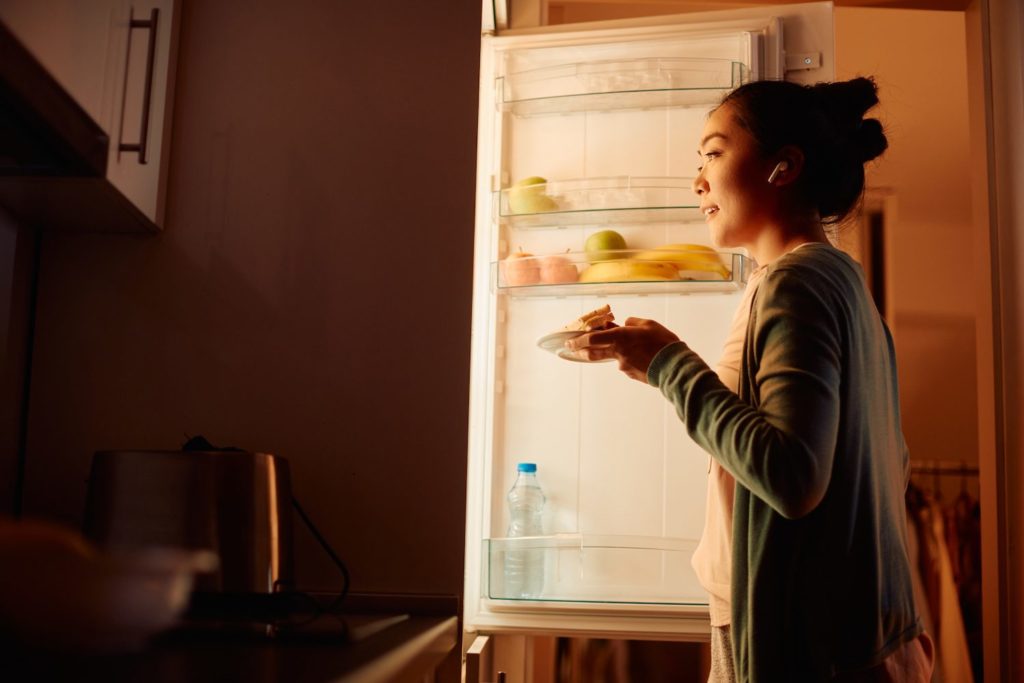 A woman stands in front of an open refridgerator in the evening