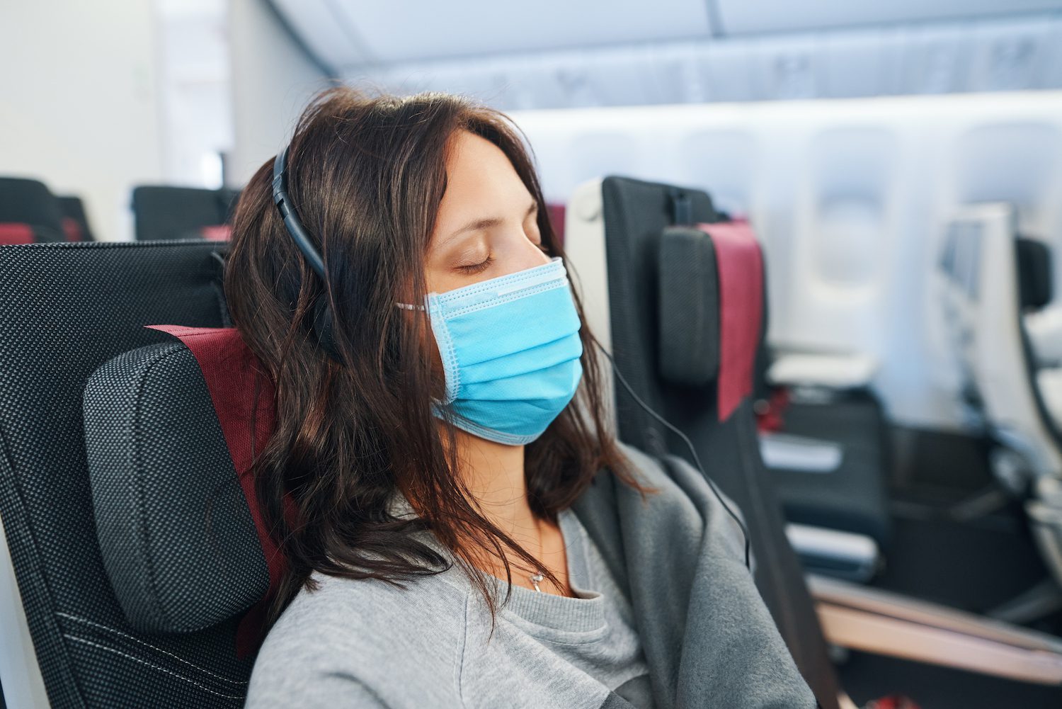 Tired woman in virus protection face mask sleeping in empty airplane