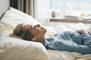 Smiling blonde woman in blue pajamas lying in bed in the morning with headphones in her ears