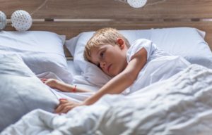 A boy struggles to fall asleep in his bed.