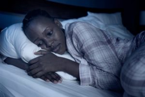 dramatic home portrait of young sick and depressed black afro American girl sitting on bed upset and sleepless at night feeling overwhelmed suffering depression and anxiety problem