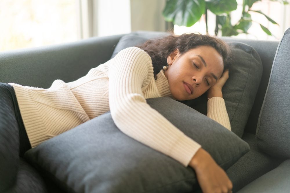 A young woman naps on a couch while hugging a pillow