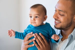 A baby is held up by their father who looks at them with a smile