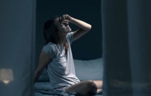 Tired woman sitting in bed at night with open window, she is suffering from the heat and she is unable to sleep