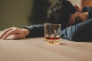 stock photo of a man sleeping beside a glass of alcohol