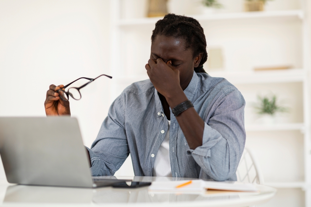 stock photo of a man tiredly rubbing his eyes while working