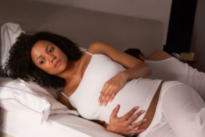 A pregnant woman holds her stomach with a contemplative look