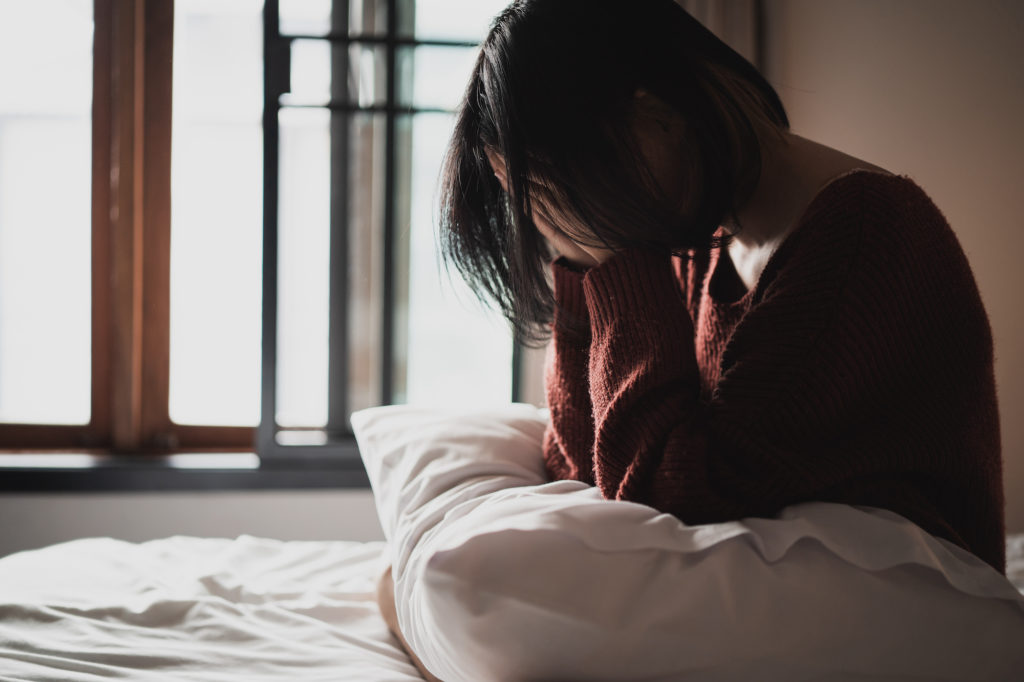 Sad woman suffering from insomnia sits alone on the bed in bedroom