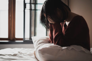 Sad woman suffering from insomnia sits alone on the bed in bedroom