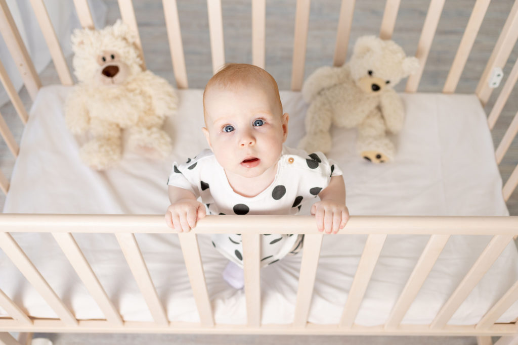 What Size Is a Crib Mattress? A baby is standing up in a crib