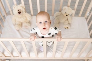 A baby is standing up in a crib