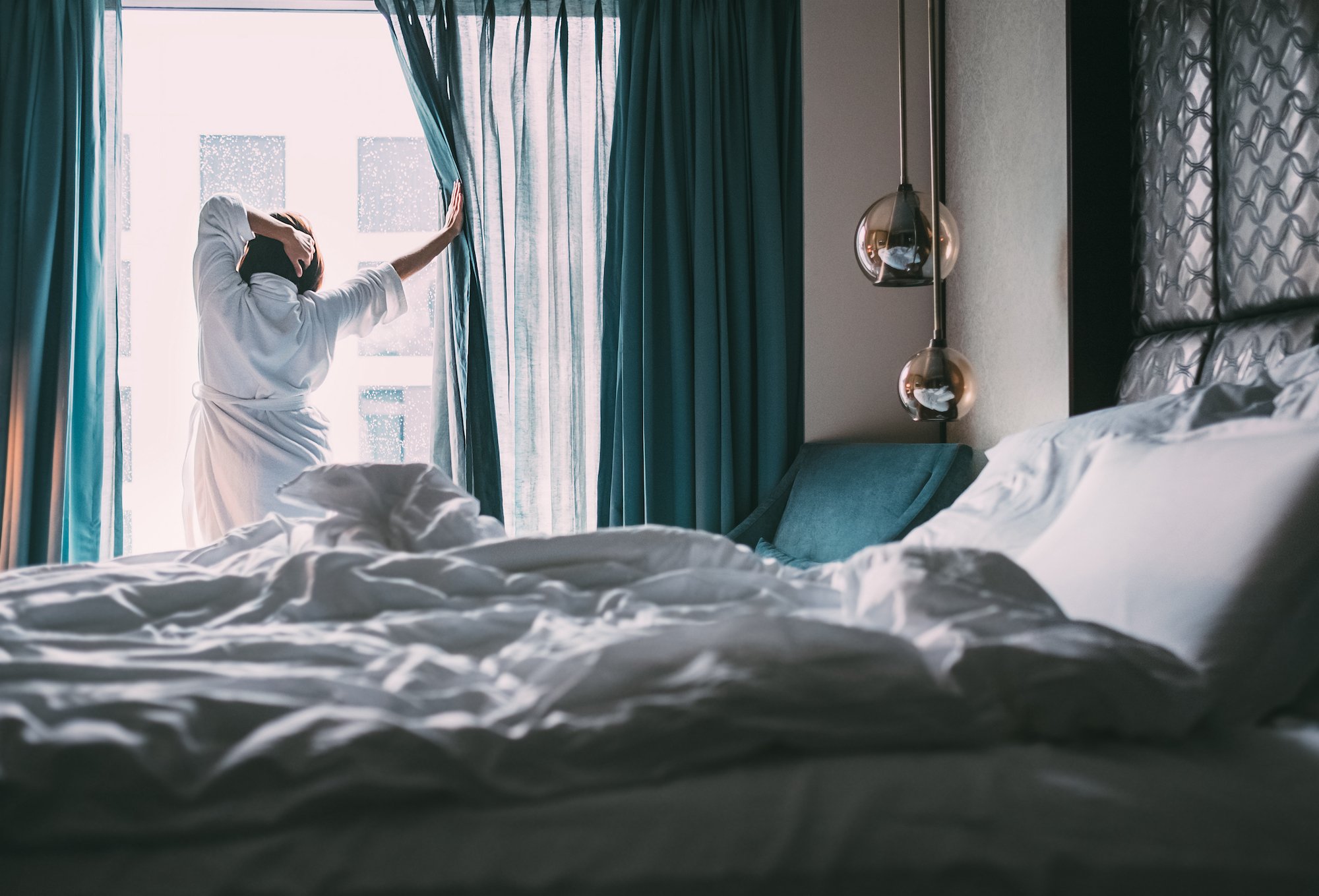 A picture of a woman standing in front of an open window in the bedroom
