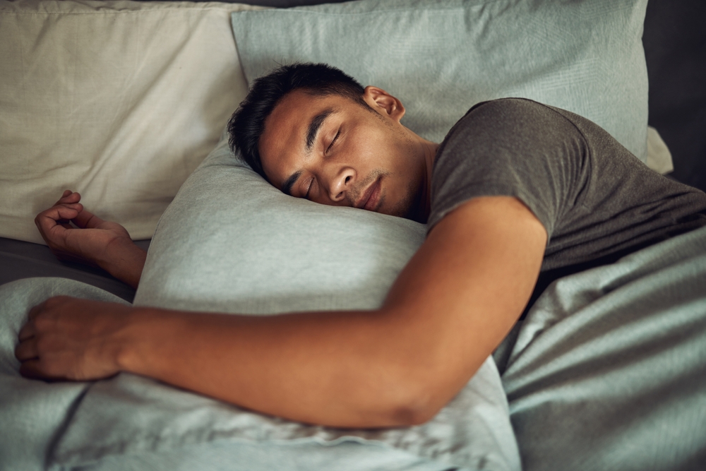 A man in deep sleep cradles pillow in arms