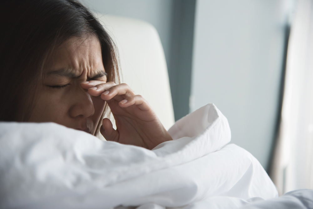 Woman rubbing her eyes with her hand while in bed