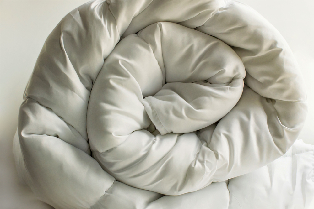 Soft white down comforter rolled on a white background