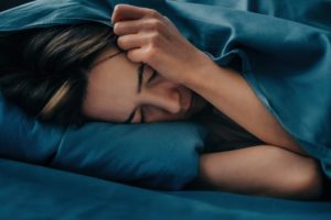 Woman lying in bed with her face covered in distress