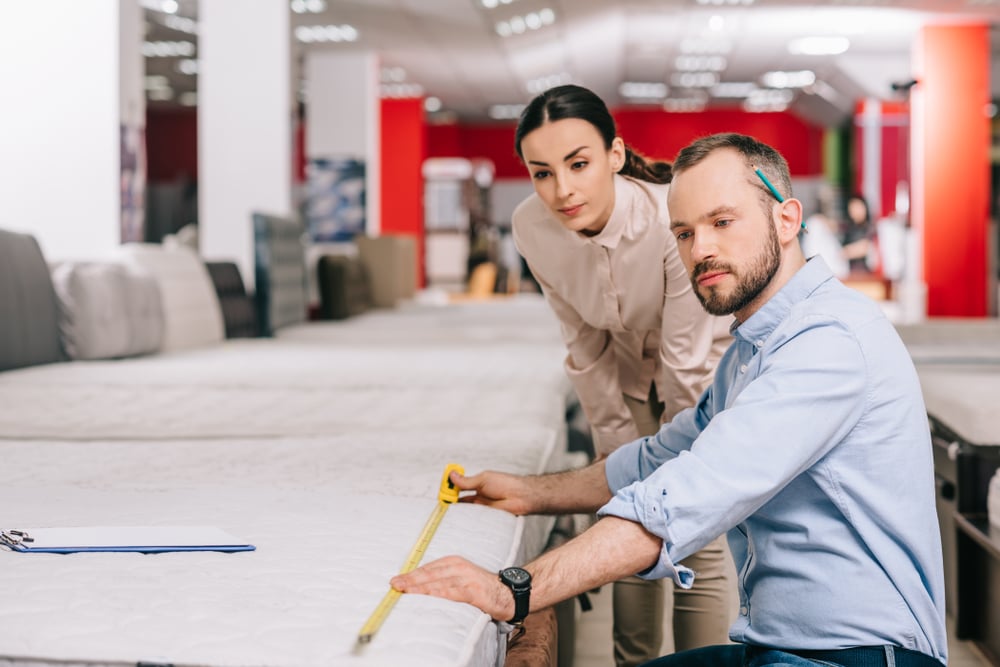 Couple measuring a mattress with measuring tape in a furniture store