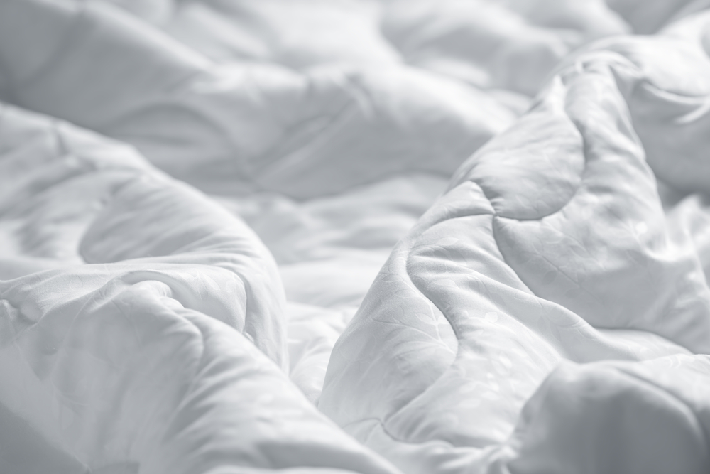 A white blanket is wrinkled on a bed