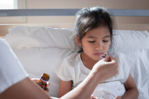 Mother giving syrup medicine on a spoon to her daughter in bed