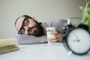 A man naps at his desk with a cup of coffee