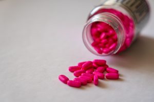 Can Benadryl Make You Sleep? Close-up of an open bottle spilling pink pills onto a surface, indicating medication use.