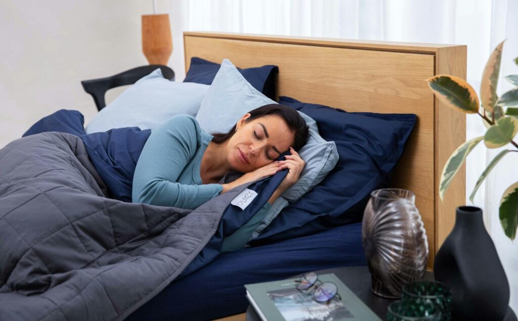 Are Weighted Blankets Hot? A woman sleeping with a weighted blanket in a blue and white bed